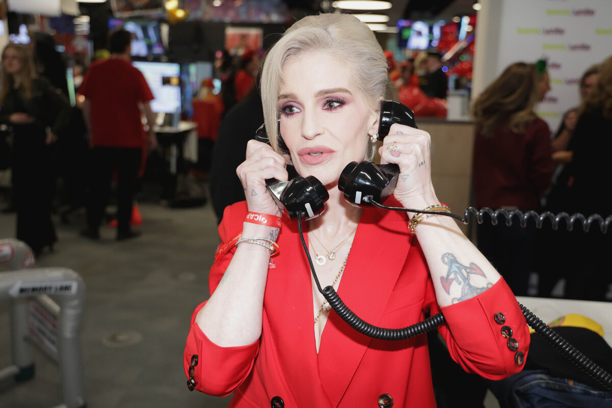 Kelly Osborne at ICAP Charity Day 2025, holding two corded telephones. She is wearing red.