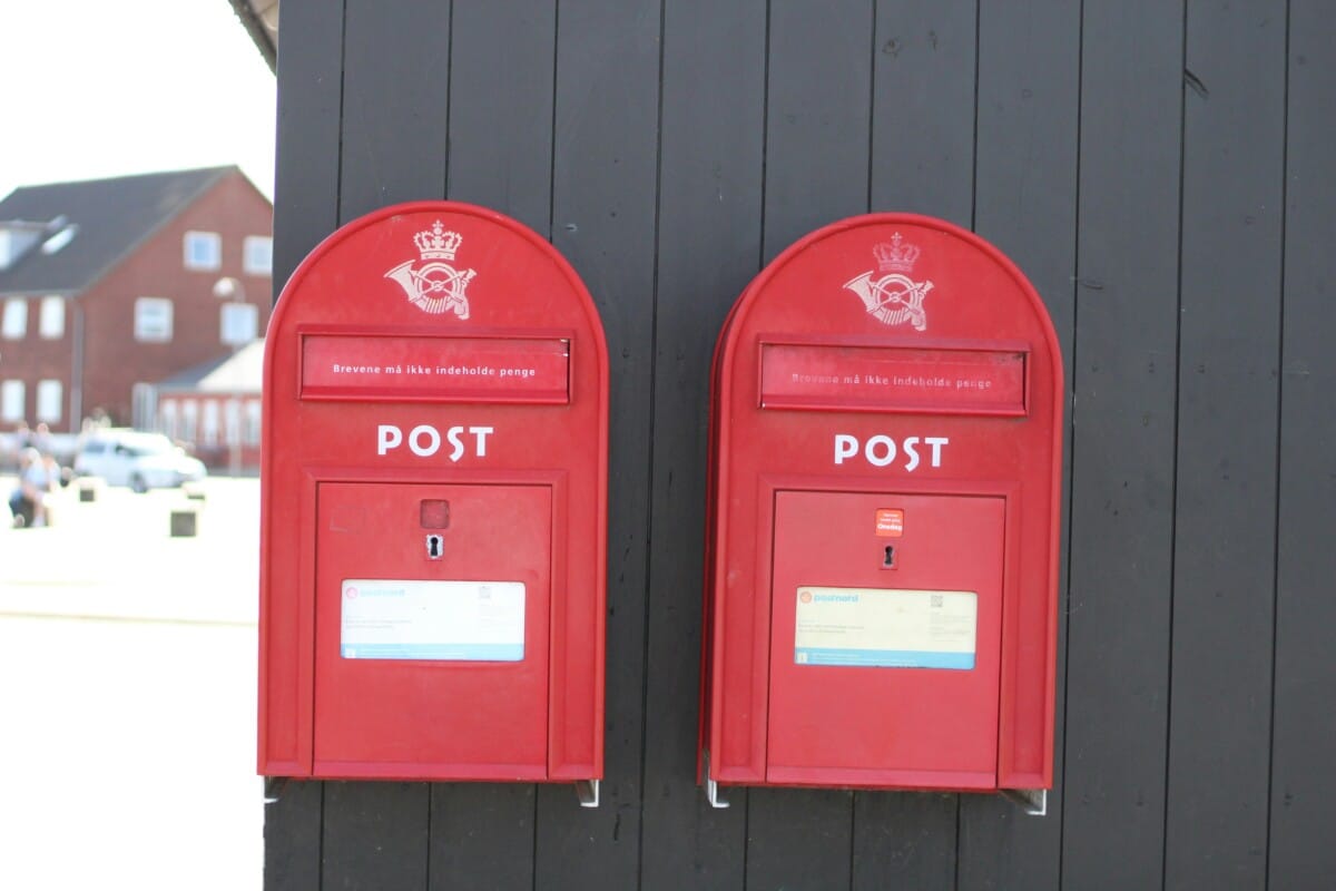 Two red Danish postboxes side by side on a wooden building in the snow.