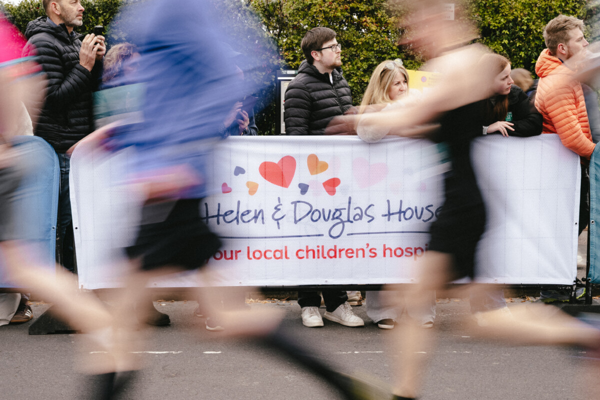 Runners running past a Helen & Douglas House banner