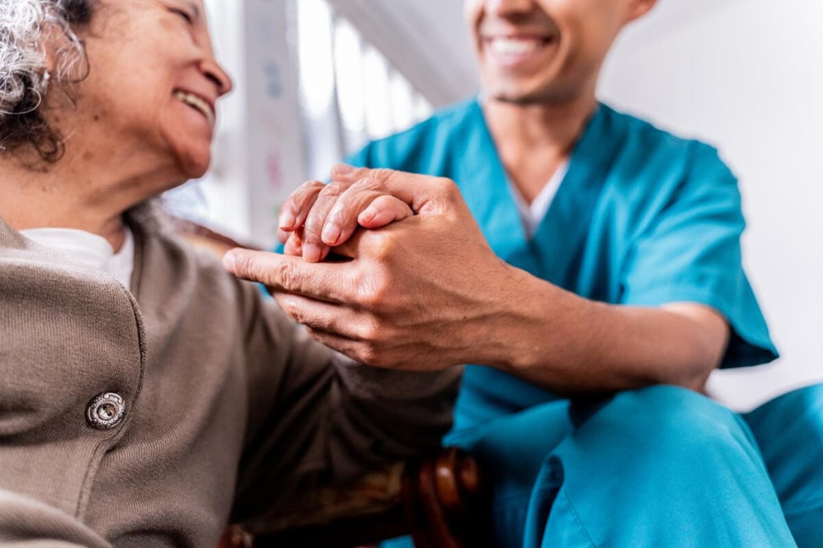 Support from the Royal Osteoporosis Society. A male nurse gently holds the hand of a woman, with both of them smiling.