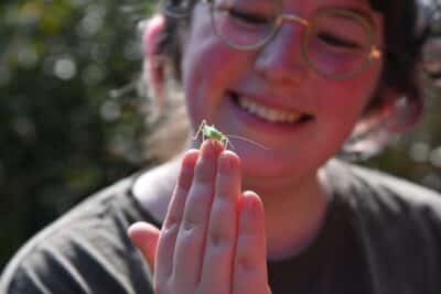 Smiling girl looks at a cricket balanced on her middle finger