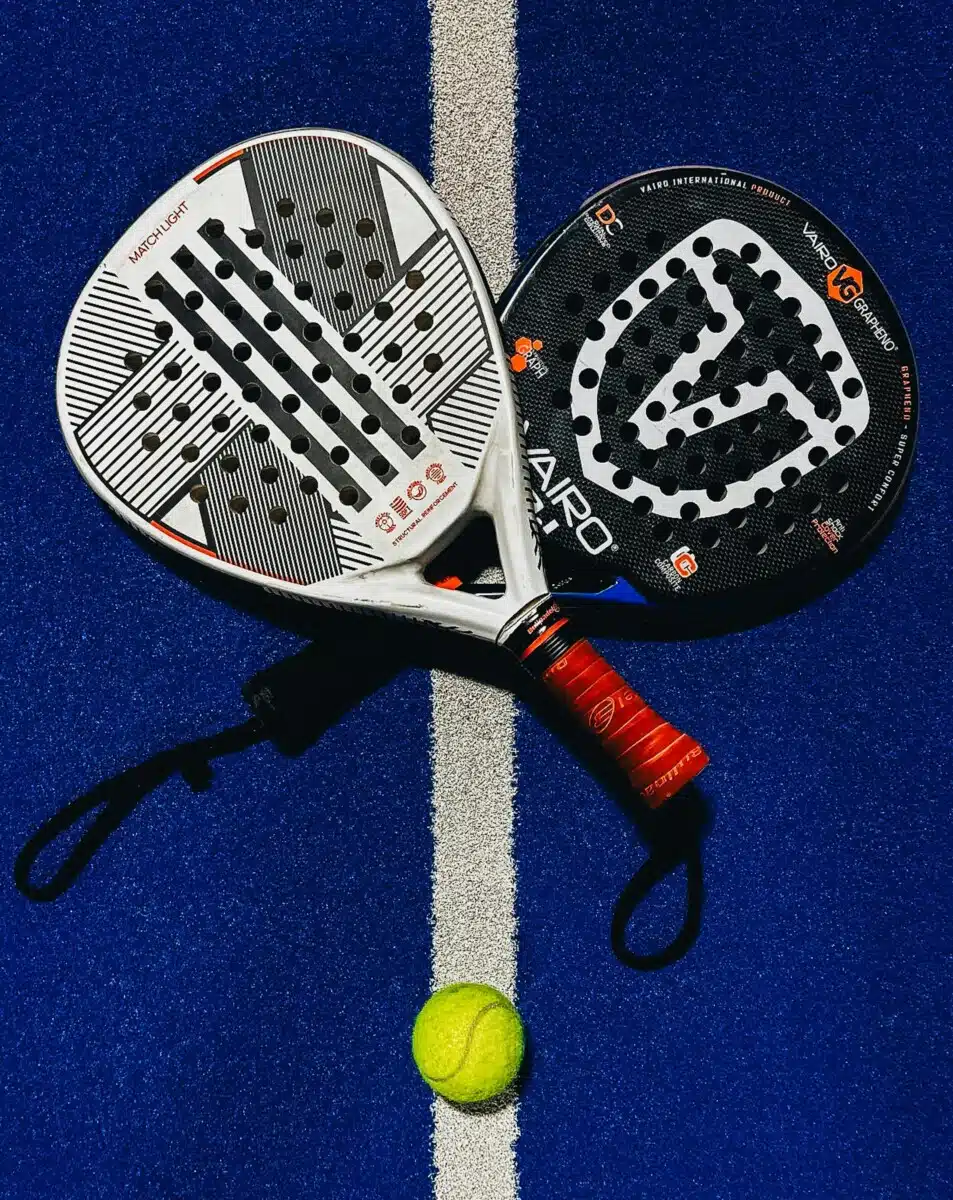 Two padel rackets and a ball placed on a white line on a vibrant blue padel court.